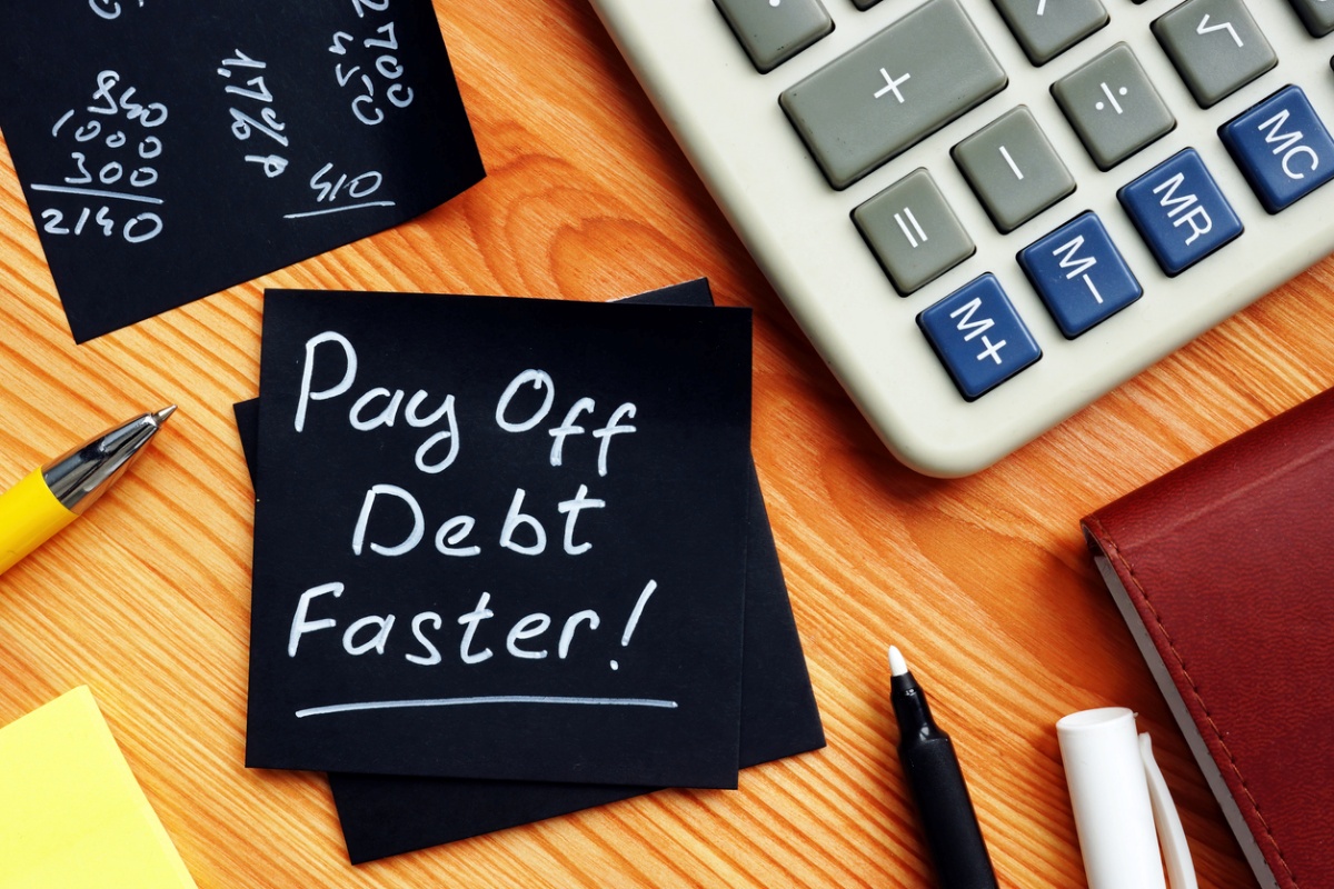 Desktop with a calculator and note saying "Pay off debt faster"